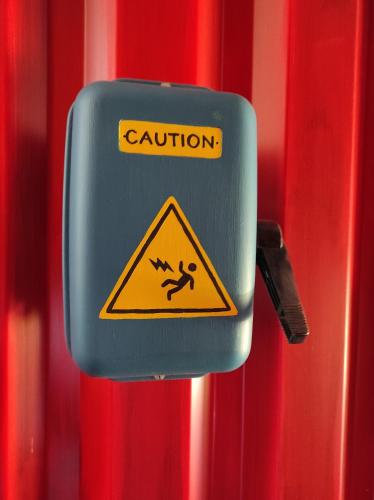 a caution sign is attached to a red wall at Apparts'hôtel la ferme du gros noyer in Malaucène