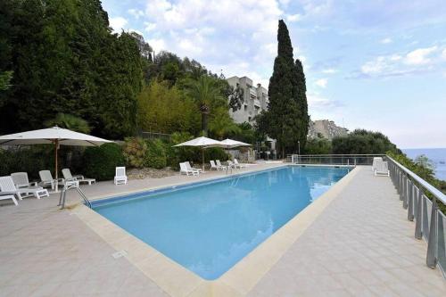 une grande piscine bleue avec chaises et parasols dans l'établissement Grand bleu, appartamento vista mare e Monaco, à Roquebrune-Cap-Martin