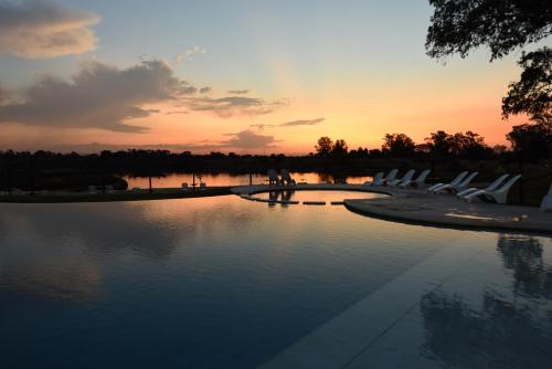 a pool with white chairs and a sunset in the background at Howard Johnson Resort & Convention Center Ezeiza in Ezeiza