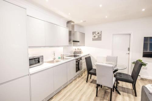 a kitchen with white cabinets and a table and chairs at EXECUTIVE APARTMENTS free on-site parking, 2 en-suites, sleeps 4, in Swindon