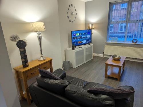 a living room with a black leather couch and a television at Station Apartments in Ashton in Makerfield