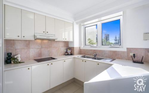 a white kitchen with white cabinets and a window at The Moroccan - QStay in Gold Coast