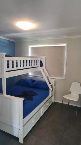 ein weißes Etagenbett in einem Zimmer mit Stuhl in der Unterkunft Banana Coast Caravan Park in Coffs Harbour