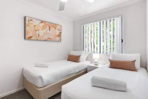 two beds in a white room with a window at MARJ12- Stylish and Spacious in Mooloolaba