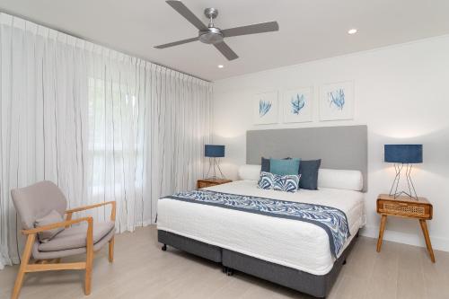 a bedroom with a bed and a chair and a ceiling fan at Mandalay Luxury Beachfront Apartments in Port Douglas