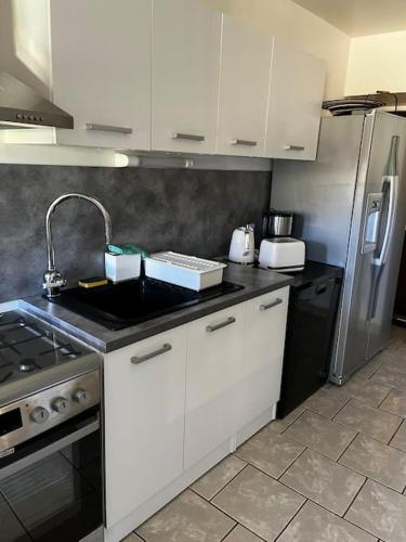 une cuisine avec des armoires blanches, un évier et un réfrigérateur dans l'établissement Petit paradis dans l'aveyron, à Saint-Jean-du-Bruel