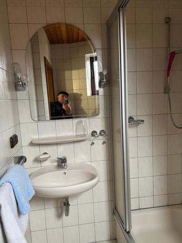 un hombre tomando una foto de un baño con lavabo y ducha en Doppelzimmer Nr 4 en Freiensteinau