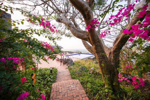 a brick pathway with pink flowers and a tree at Victoria Nui Sam Lodge in Chau Doc