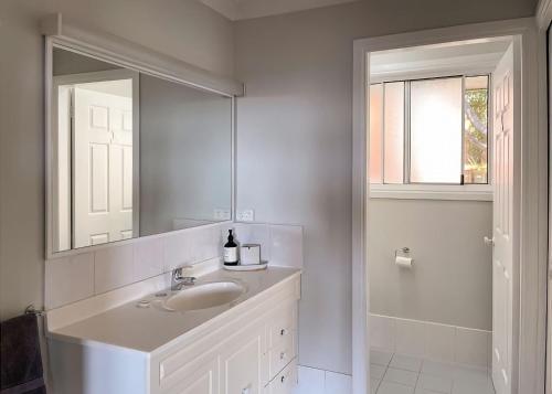 een witte badkamer met een wastafel en een spiegel bij On the Hillside in Coffs Harbour