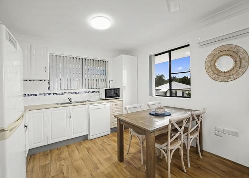 a white kitchen with a wooden table and chairs at Blue Gem in Sawtell