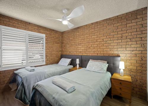two beds in a room with a brick wall at Driftwood Court 1 in Sawtell
