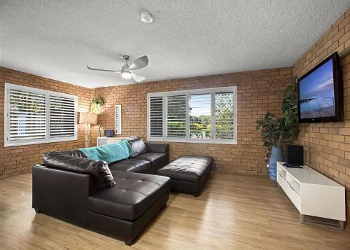 a living room with a leather couch and a flat screen tv at Driftwood Court 1 in Sawtell