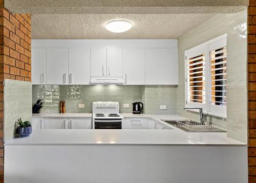 a white kitchen with white cabinets and a sink at Driftwood Court 1 in Sawtell