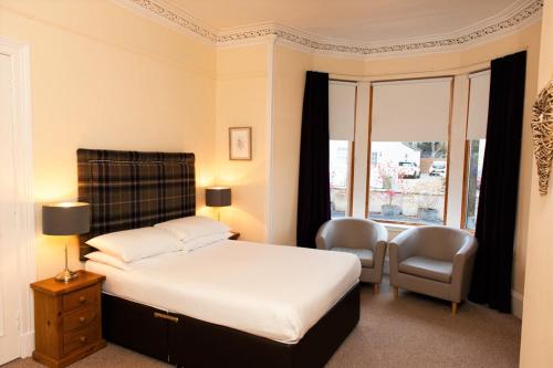 a bedroom with a bed and two chairs and a window at Alban and Abbey House in Inverness