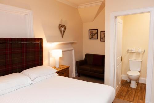 a bedroom with a bed and a chair and a toilet at Alban and Abbey House in Inverness