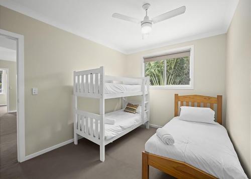 a bedroom with a bunk bed and a white bed and a window at Sawtell Swells in Sawtell