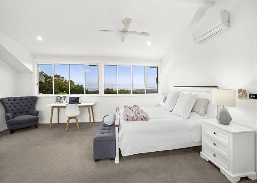 a white bedroom with a bed and a desk and a chair at Sea Breeze in Coffs Harbour