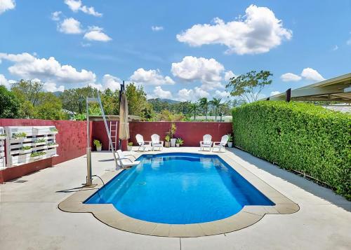 a swimming pool with two chairs and a hedge at McCabe Coffs Retreat in Coffs Harbour