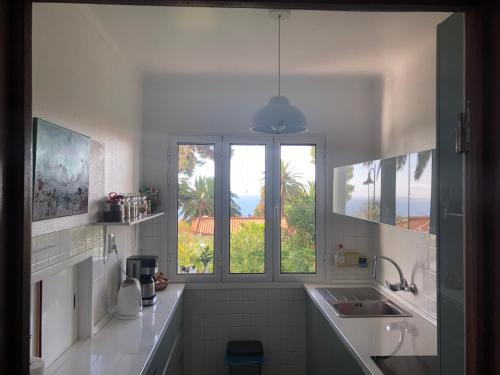 a white kitchen with a sink and two windows at Casa Palmeira - Ferienhaus mit Meerblick in Caniço