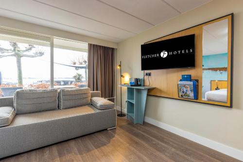 a hotel room with a couch and a flat screen tv at Fletcher Hotel Restaurant Loosdrecht-Amsterdam in Loosdrecht