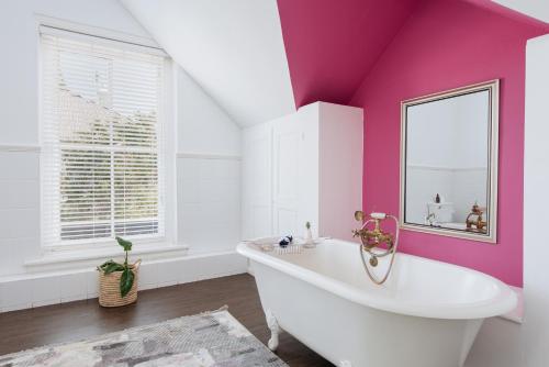 Baño de color rosa con bañera y espejo en River Manor Boutique Hotel by The Living Journey Collection, en Stellenbosch