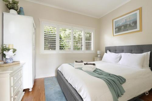 a bedroom with a large white bed and two windows at Camellia Cottage in Wentworth Falls