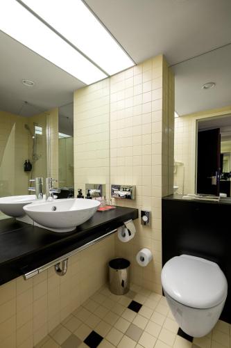 a bathroom with two sinks and a toilet and a mirror at Ramada Plaza by Wyndham Bucharest Convention Center in Bucharest