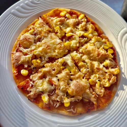 a pizza with cheese and corn on a white plate at Amaira Resort & Farms - Mirik, West Bengal in Mirik