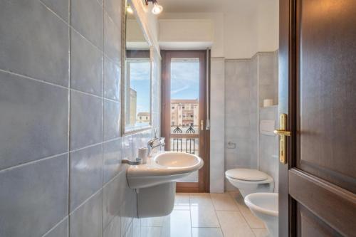 Un baño con lavabo, inodoro y ventana. en Dimoras Ampio Appartamento Centrocittà, en Olbia