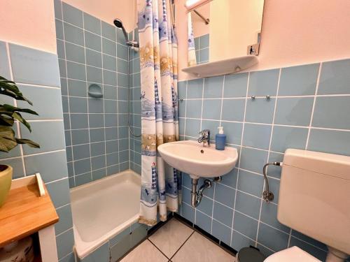 La salle de bains est pourvue de carrelage bleu, d'un lavabo et de toilettes. dans l'établissement Haus Atlantic Whg. 212, à Cuxhaven