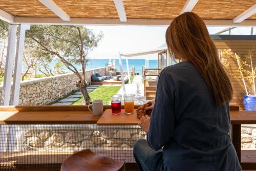 a woman sitting at a table looking out at the ocean at Junam Private Beachfront Cabins in Agios Nikitas