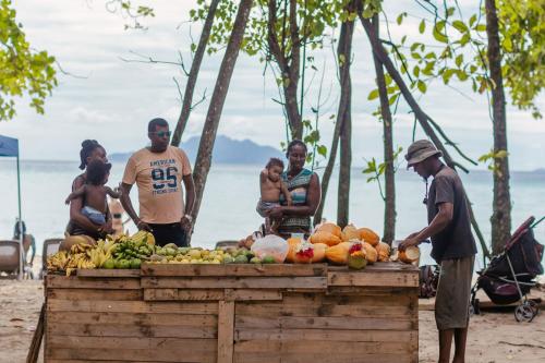 a group of people standing around a fruit stand on the beach at STORY Seychelles in Beau Vallon