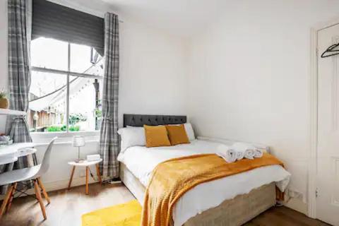 倫敦的住宿－Alross Room with Breakfast，一间卧室配有一张床、一张书桌和一个窗户。
