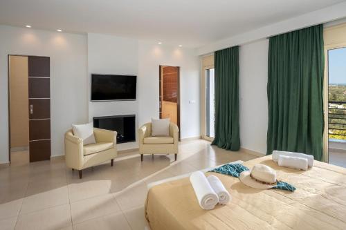 a bedroom with a bed and two chairs and a television at Villa Melissa by Estia in Hersonissos
