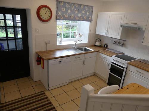 a kitchen with white cabinets and a clock on the wall at Pant Glas in Penmaen-mawr