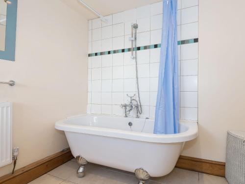 a bath tub with a blue shower curtain in a bathroom at Lazy Cottage in Haverigg