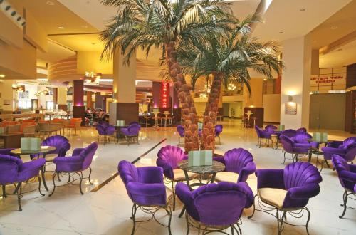 a hotel lobby with purple chairs and palm trees at Limak Lara Deluxe Hotel & Resort Antalya in Lara
