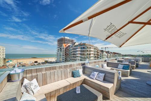 a patio with benches and an umbrella and the beach at The Memlinc in Knokke-Heist