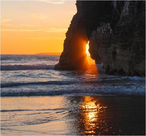 a beach with a rock arch in the ocean at sunset at Rooms at The Marine in Ballybunion