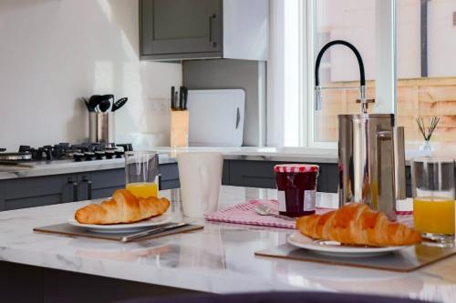 a kitchen counter with two plates of croissants and orange juice at Causey Lodge superb comfy home in Exeter by StayStay in Exeter