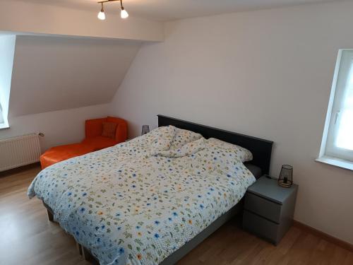 een slaapkamer met een bed en een oranje stoel bij Lillie 3-4 Personen - Ferienwohnungen Wagner & Gaul Falkenauel in Falkenauel