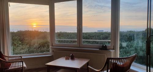 a table and chairs in a room with two windows at Zee en Duin in Cadzand