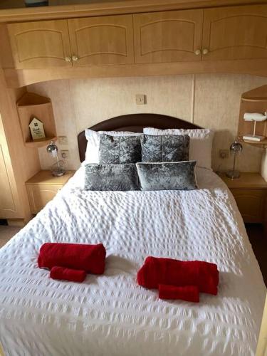 a white bed with two red pillows on it at No29 at Three Lochs Holiday Park in Balminnoch