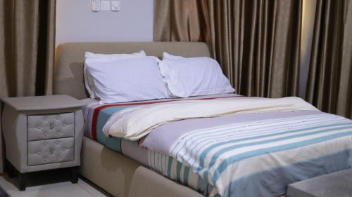 een bed met witte lakens en een nachtkastje naast een raam bij Jeffston Court Apartments in Accra