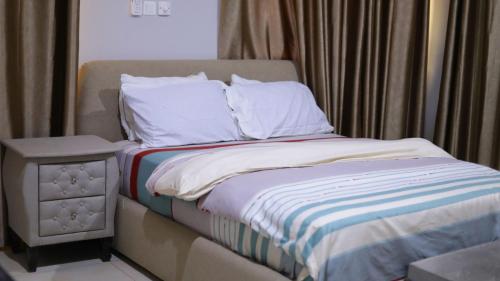 a bed with white sheets and a night stand next to a window at Luxury 3BR Apartment in Ghana Jeffston Court Accra Prime Location & Comfort in Accra