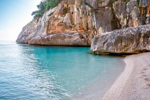 a beach next to a large rocky cliff at Le Corti Sarde Countryside in Bari Sardo