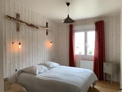 sypialnia z białym łóżkiem z czerwoną zasłoną w obiekcie Charmante Maison de Campagne en Pierres et Bois w mieście Sartilly