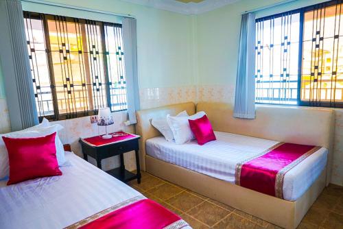 a bedroom with two beds with pink pillows and windows at Angkor Sunshine Oasis in Siem Reap