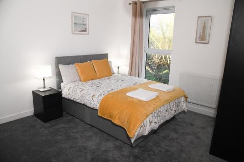 ein Schlafzimmer mit einem Bett mit orangefarbenen Kissen und einem Fenster in der Unterkunft Crayford, Super Cosy 2-Bed Apartment in Dartford
