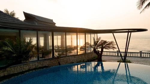 a house with a swimming pool next to the ocean at Dankbaar Resort Quy Nhon in Quy Nhon